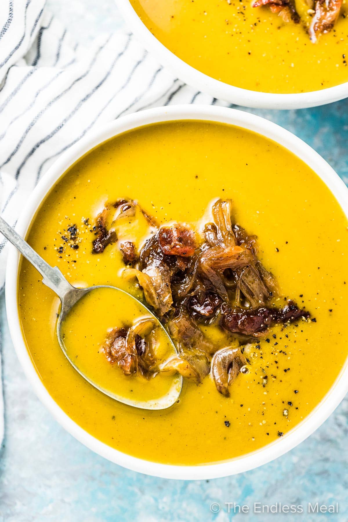 A white bowl with a spoon in it filled with a pumpkin fall soup recipe and topped with maple bacon onions.