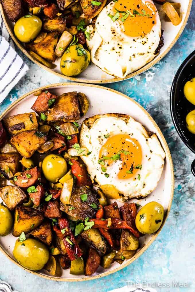 Two plates filled with Spanish breakfast potatoes and a fried egg.