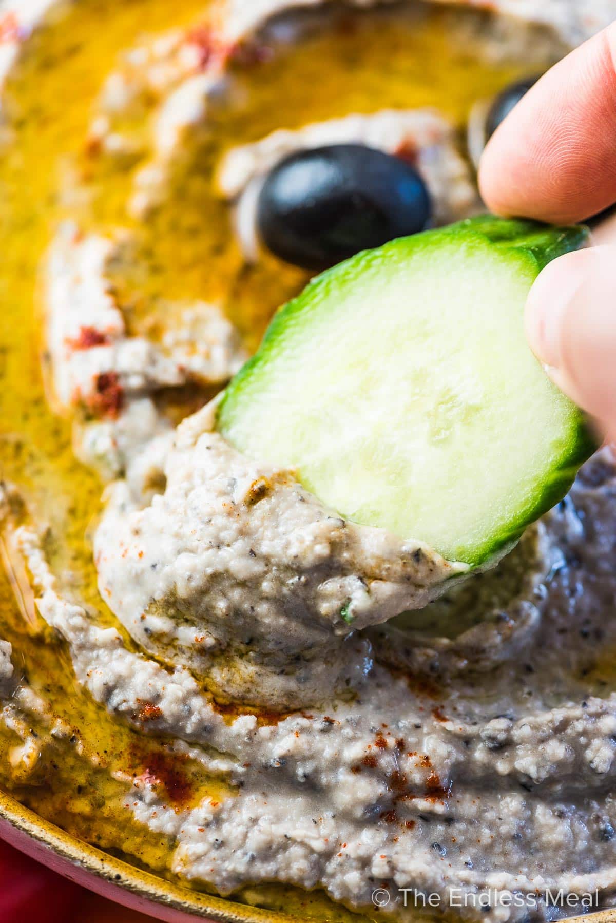 A cucumber slice scooping up some white bean dip with olives.