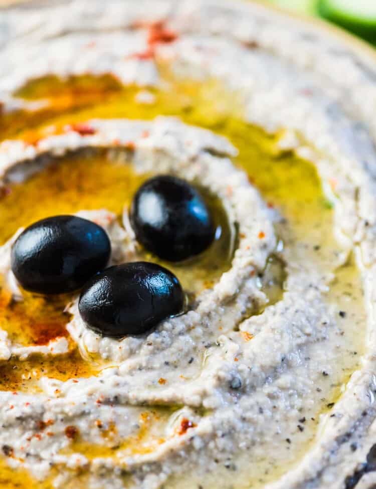 A close up of this white bean dip in a bowl with a few olives on top.