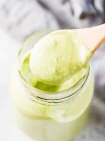 A spoon taking a scoop out of a glass jar of avocado ranch dressing.