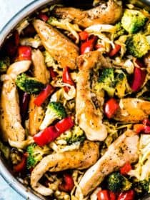 A frying pan full of chicken cabbage stir fry with red peppers and broccoli.