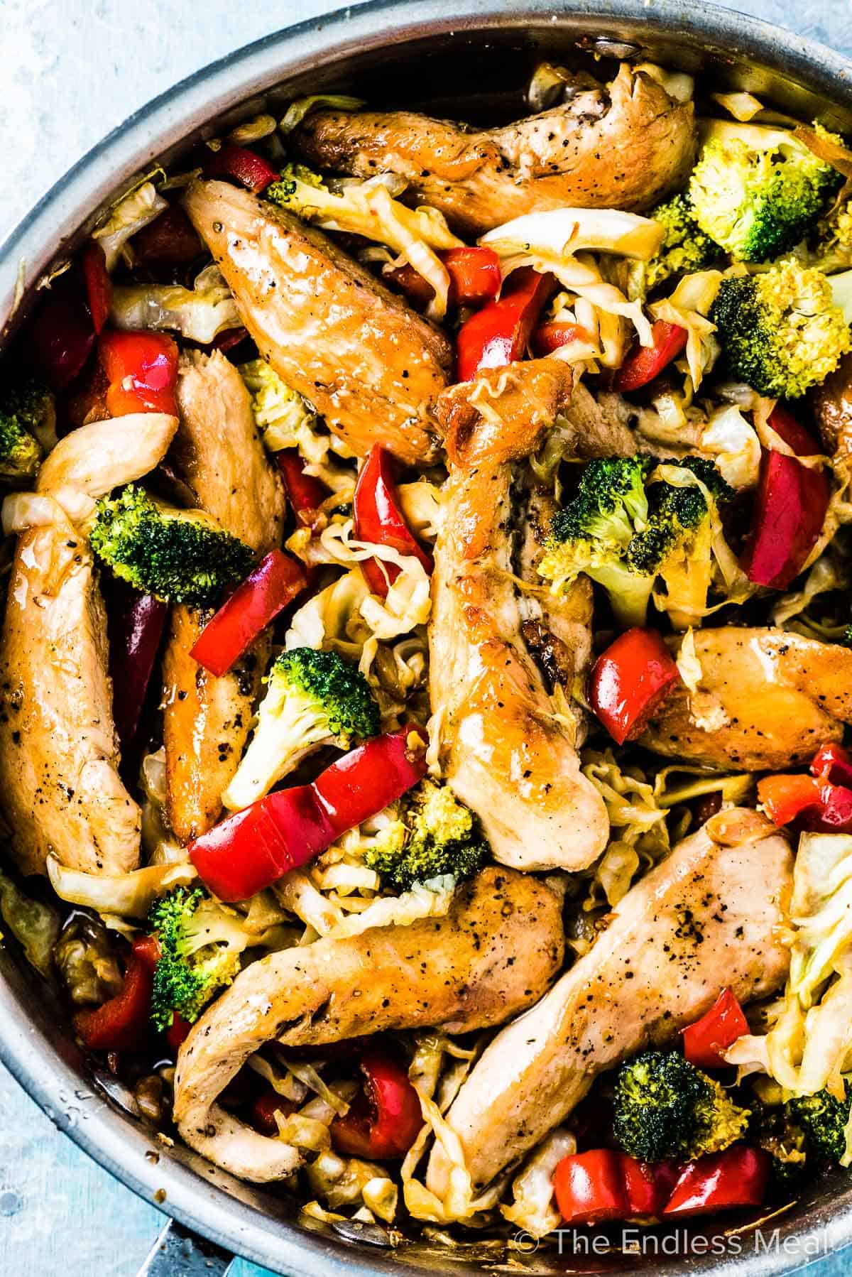 A frying pan full of chicken cabbage stir fry with red peppers and broccoli for one of our healthy recipes for dinnertime