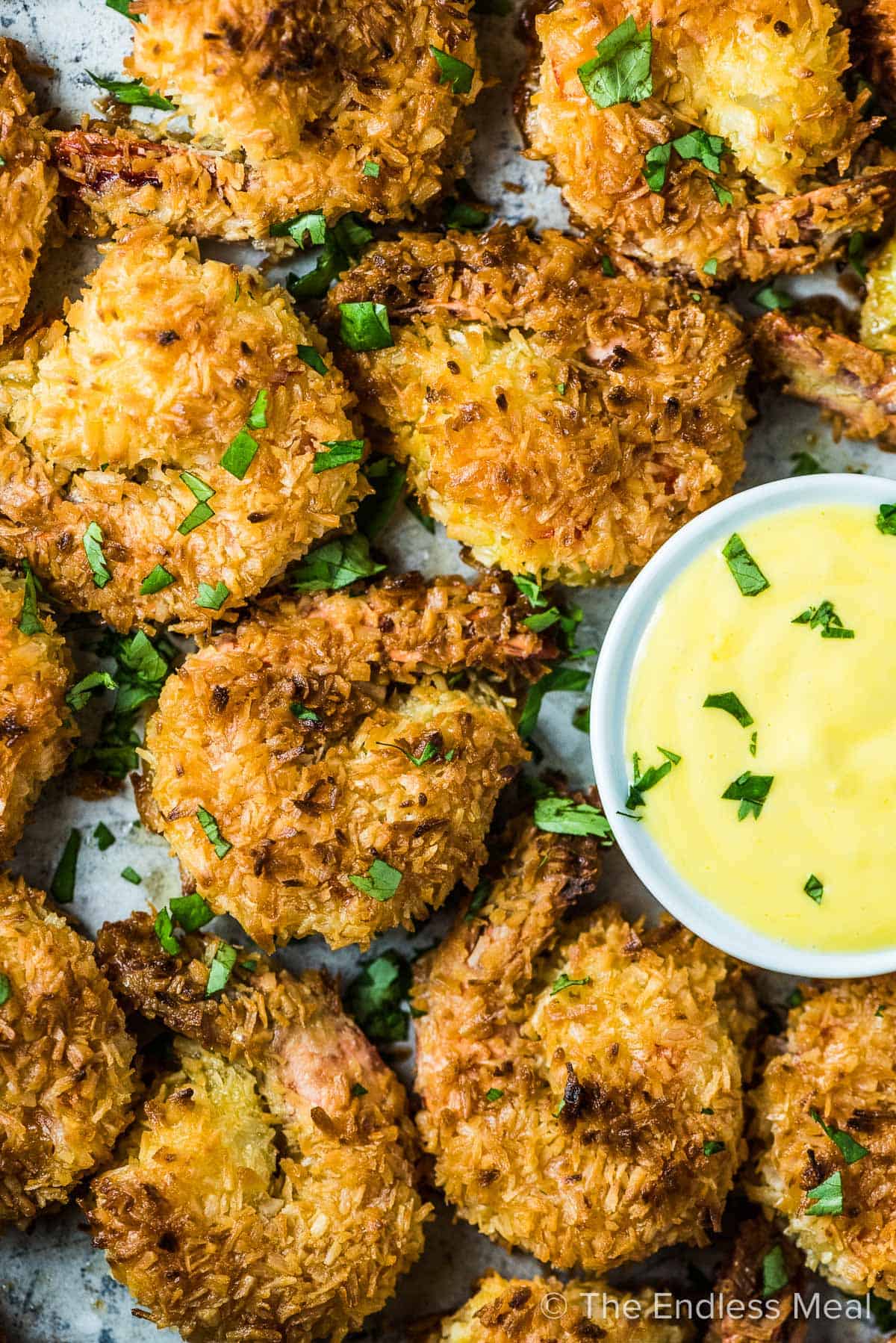 A baking tray filled with crispy coconut shrimp and a bowl of mango sauce. 
