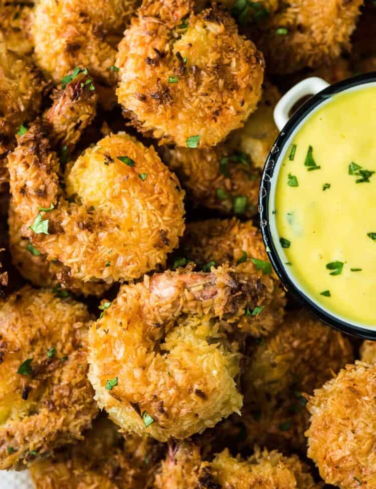 A close up of a plate of crispy coconut shrimp with mango dipping sauce on the side.