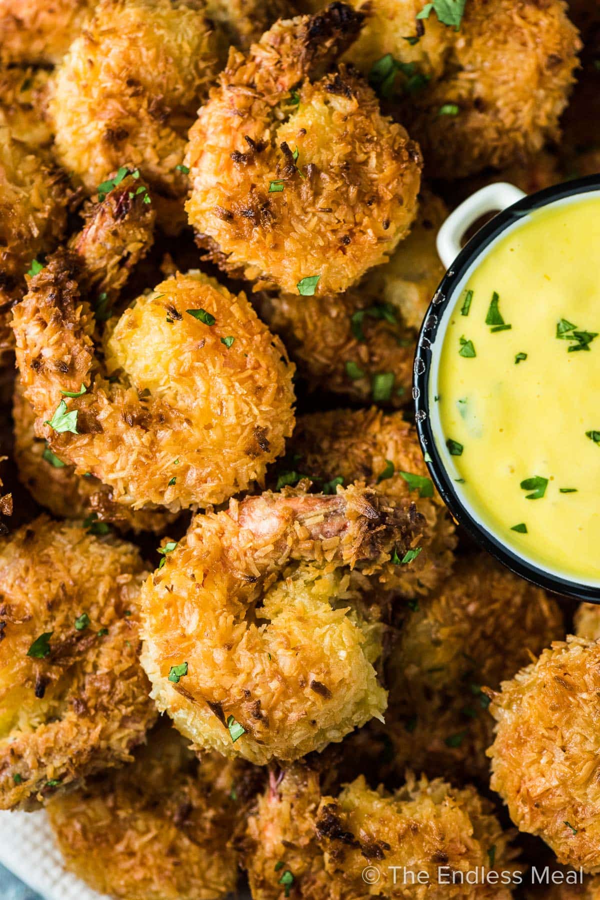 A close up of a plate of crispy coconut shrimp with mango dipping sauce on the side. 