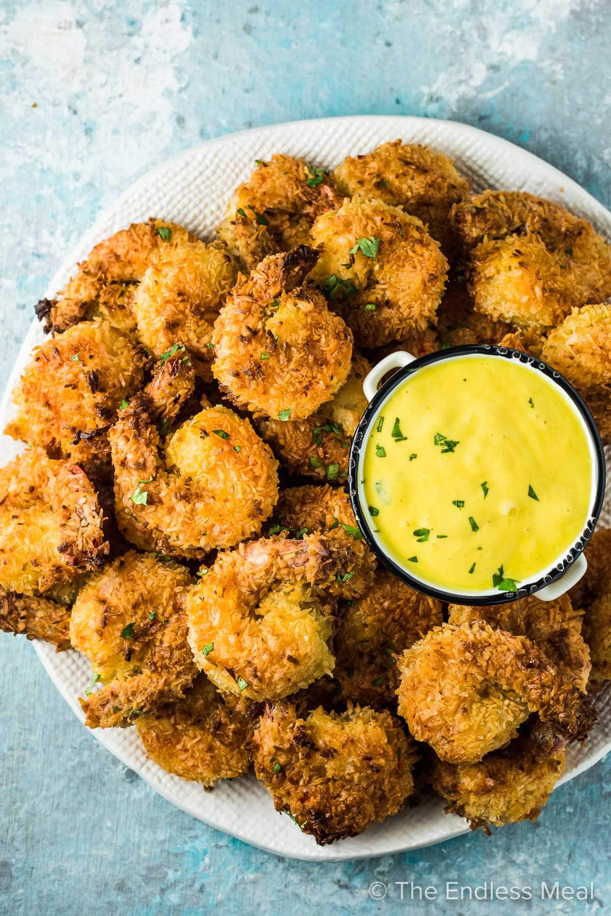 A big pile of coconut shrimp on a white plate with a side of mango dipping sauce.