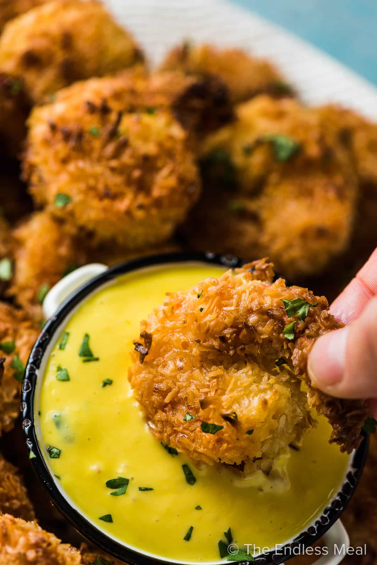 A hand dipping a coconut shrimp into a bowl of mango dipping sauce.