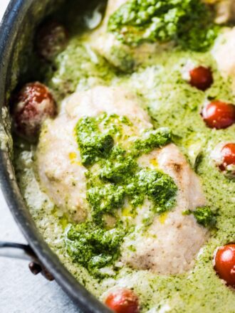 A close up of creamy pesto chicken in a pan with some cherry tomatoes.