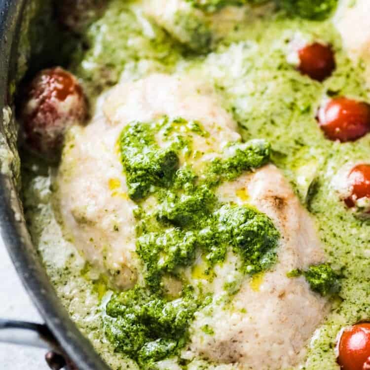 A close up of creamy pesto chicken in a pan with some cherry tomatoes.