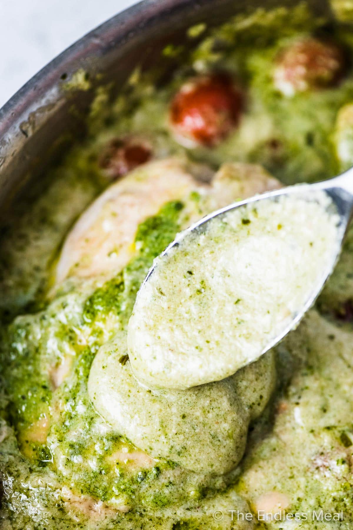 A close up of the creamy pesto sauce being poured over a chicken breast.