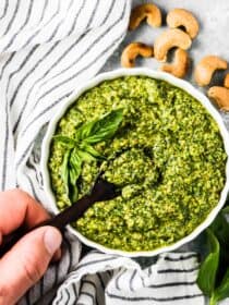 A hand holding a spoon taking a scoop of dairy free pesto out of a white bowl.