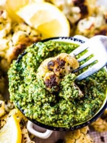 A piece of Italian cauliflower on a fork being dipped into pesto.