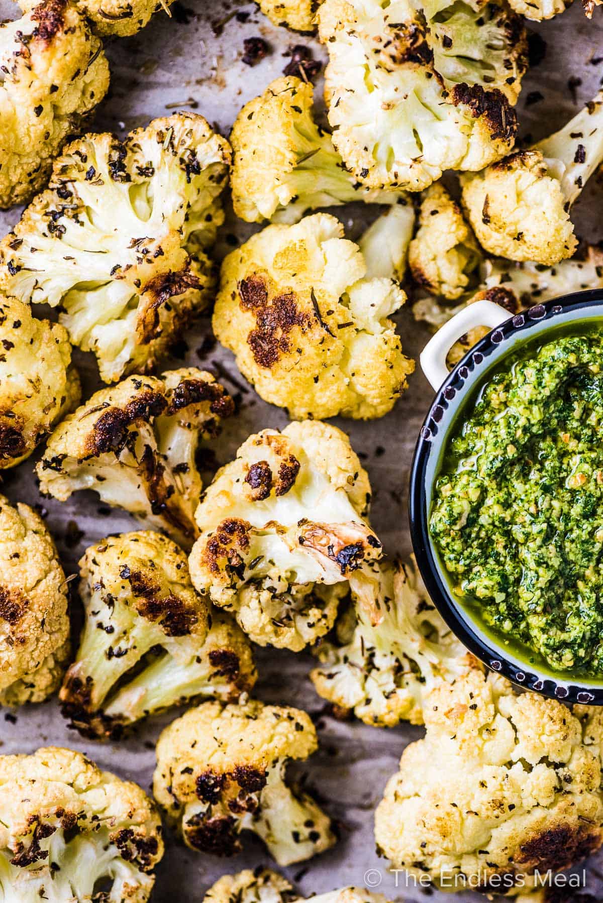 A close up of italian roasted cauliflower on a baking sheet with pesto on the side.