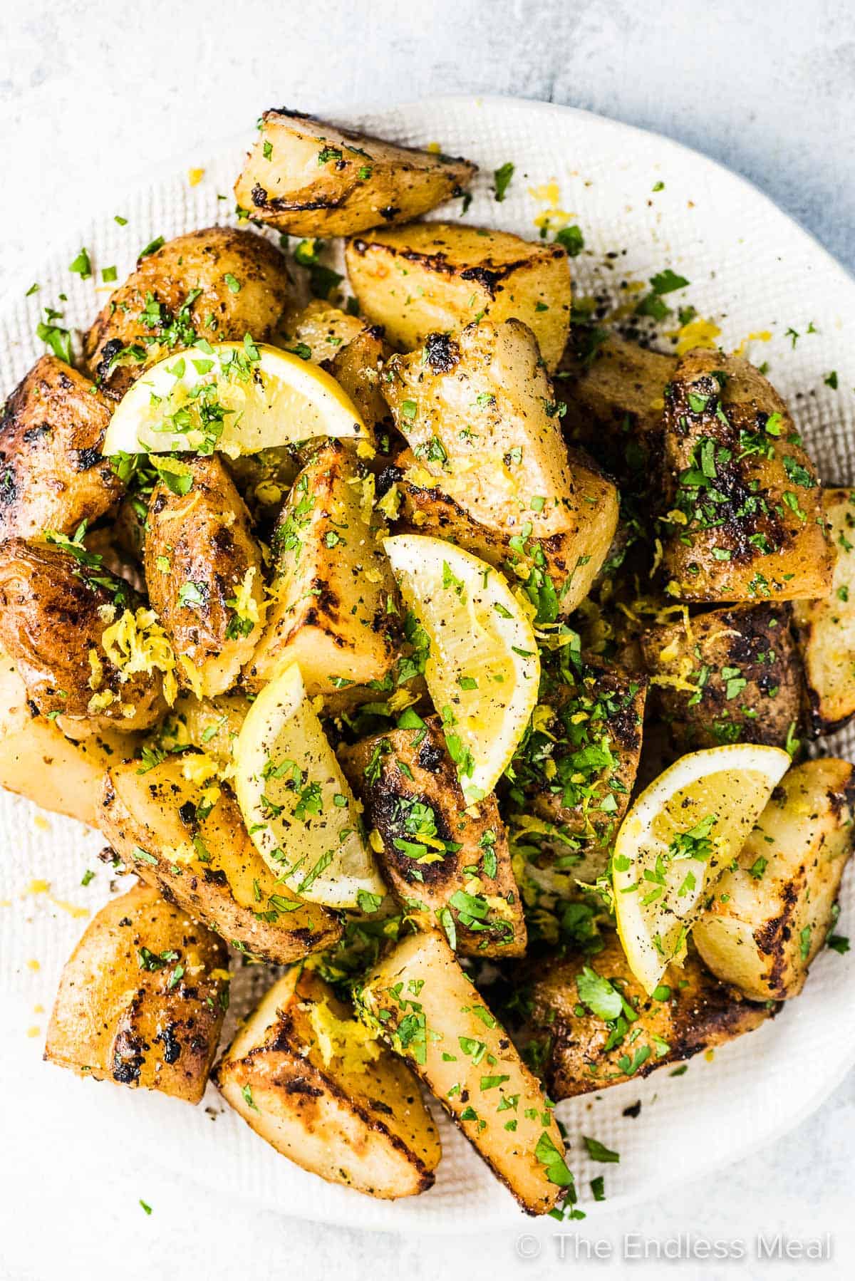 Lemon potatoes in a white serving bowl with lemons and parsley on the top.