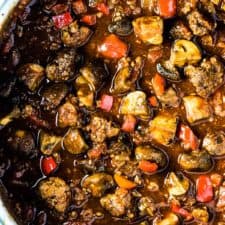 A big pot of sausage chili with lots of sausage chunks and mushrooms in it.