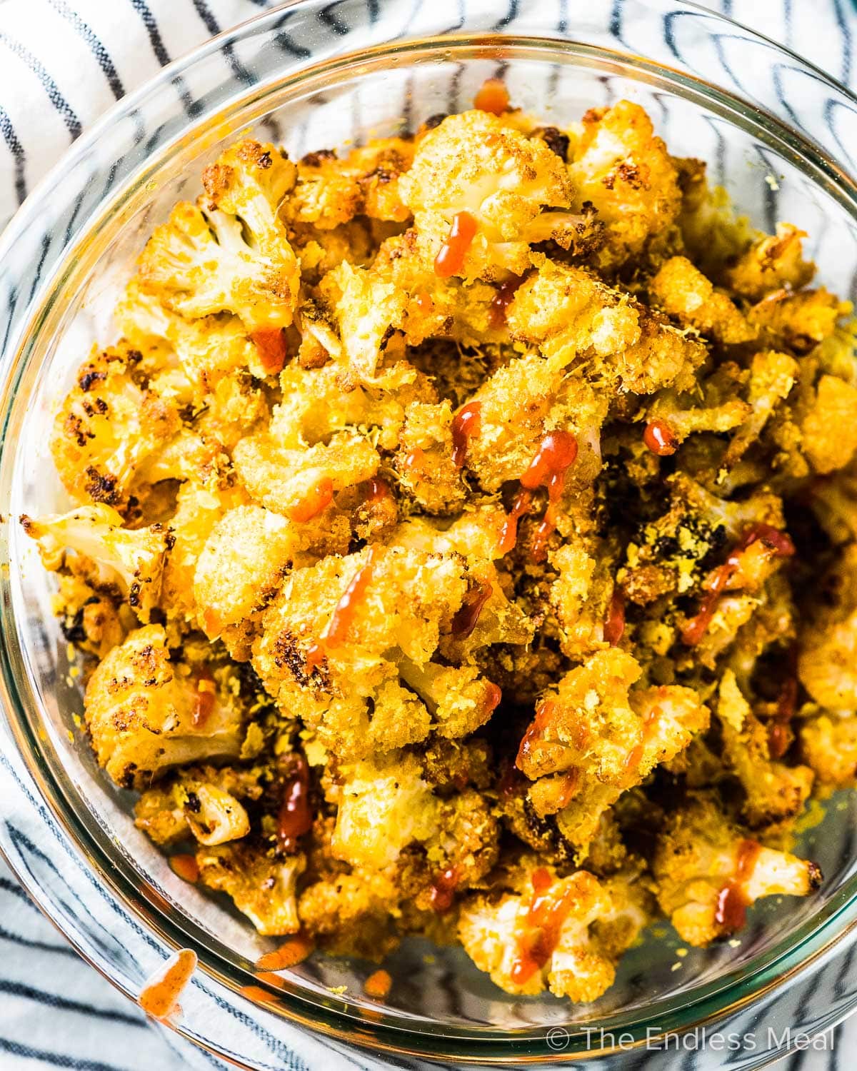 Cauliflower popcorn in a glass bowl with a little sriracha over the top.