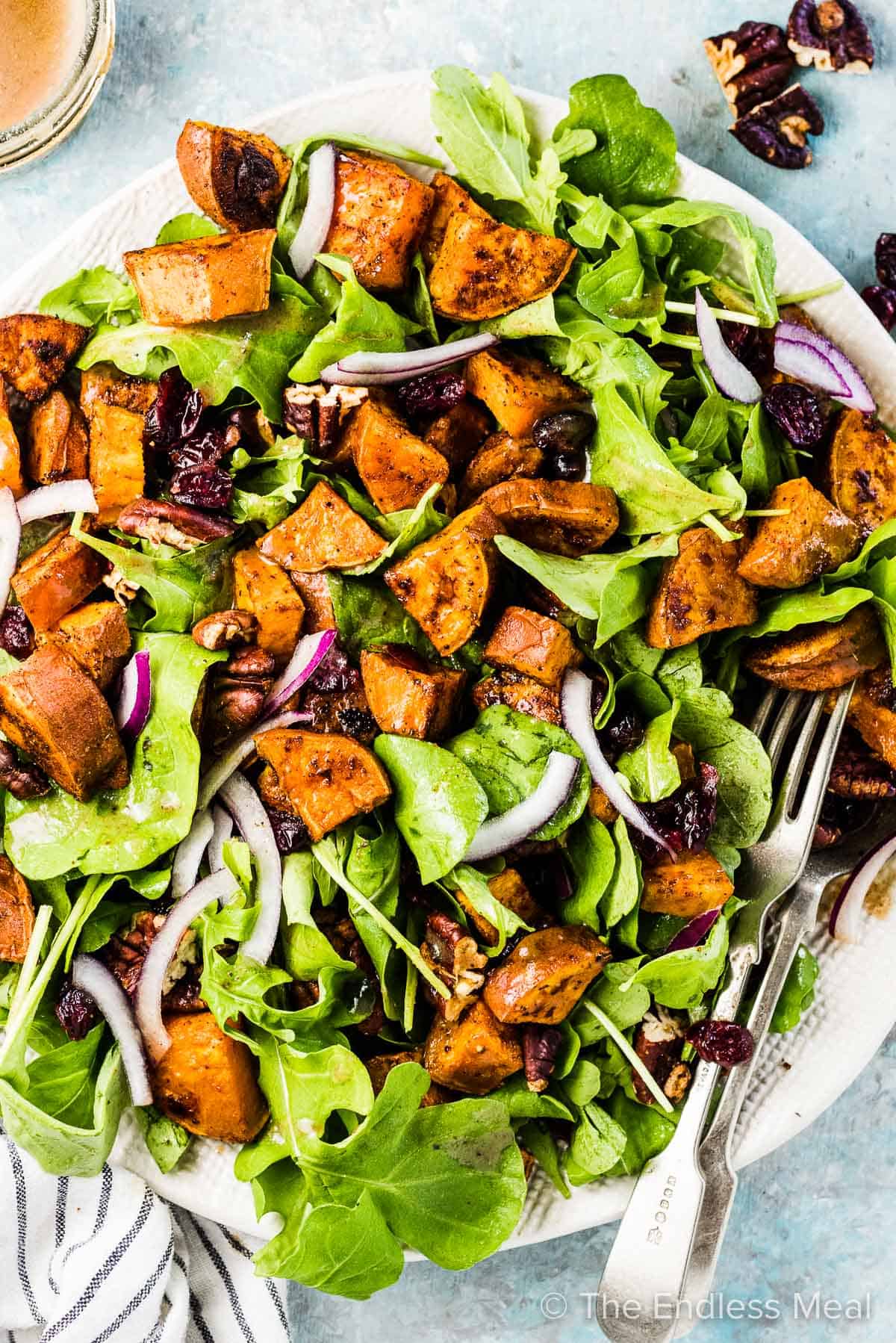 A big, white bowl filled with arugula and sweet potato salad on a blue table. 
