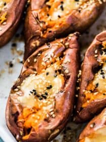 A close up of a baked sweet potato cut open with miso tahini butter on top and a sprinkle of sesame seeds.