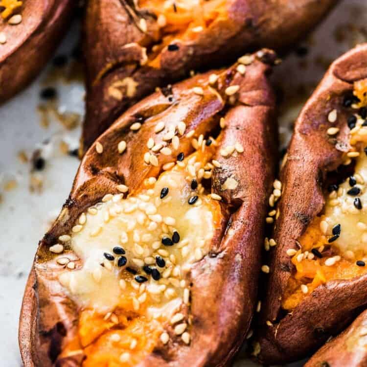 A close up of a baked sweet potato cut open with miso tahini butter on top and a sprinkle of sesame seeds.
