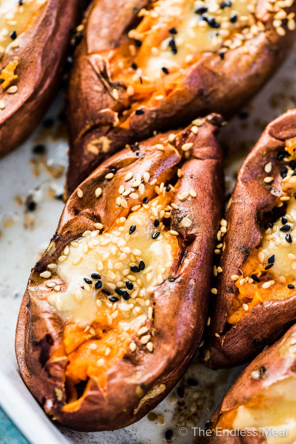A close up of a roasted sweet potato cut open with miso tahini butter on top and a sprinkle of sesame seeds. 