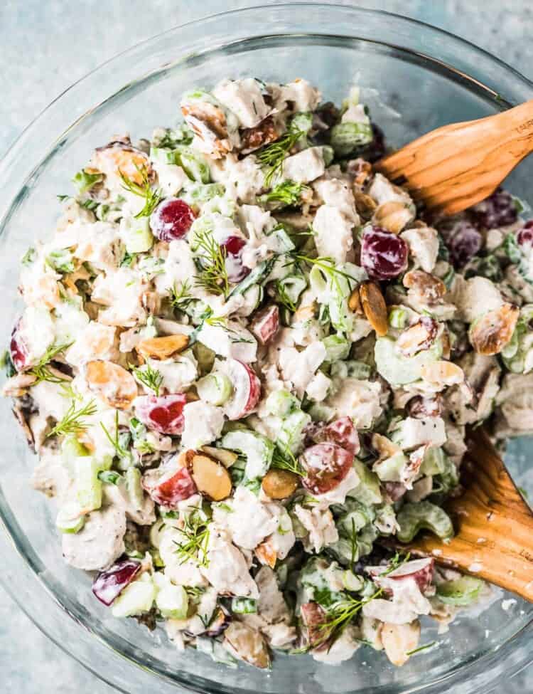 This chicken salad recipe in a glass bowl with wooden salad spoons.
