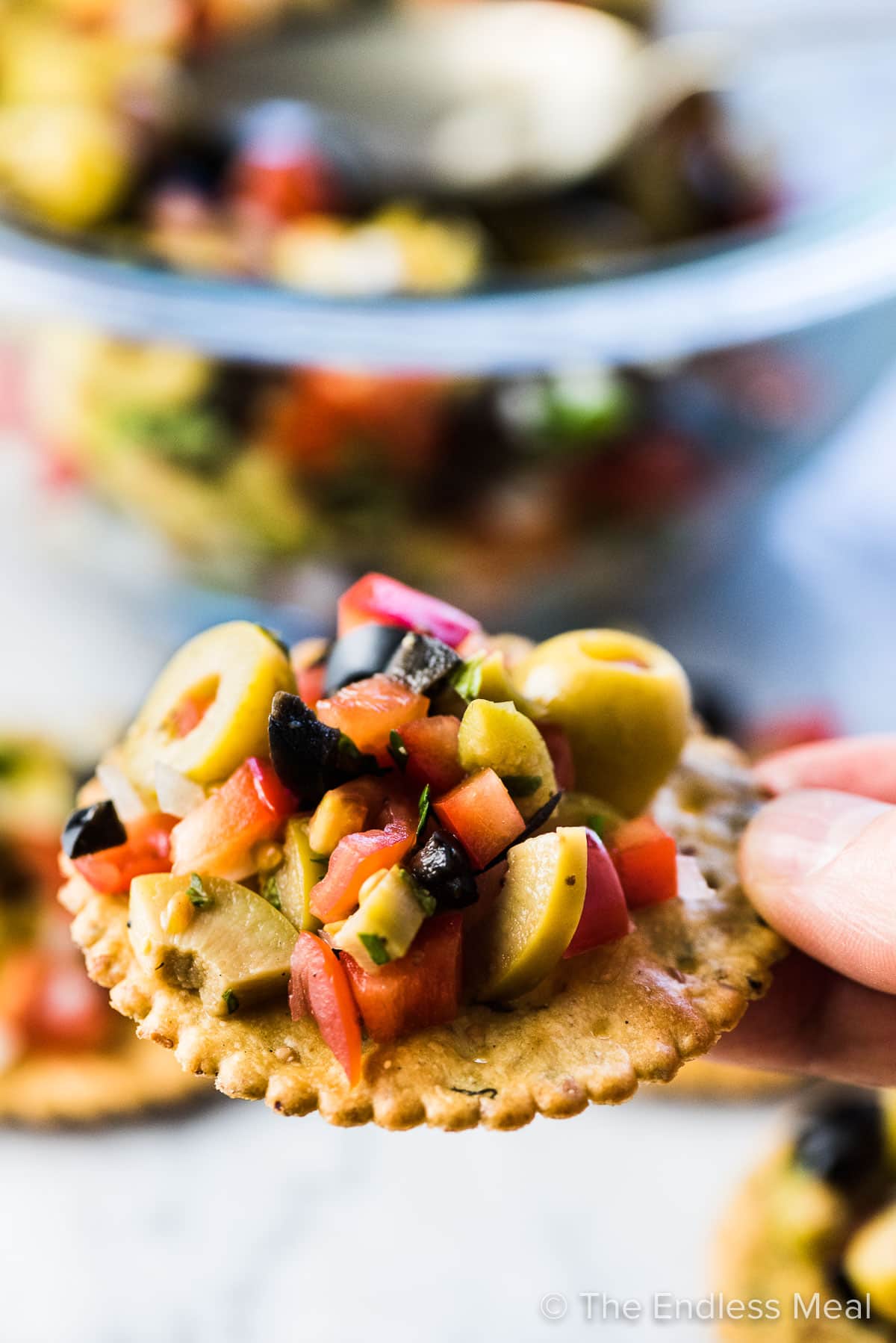 A hand holding a cracker piled with olive salsa.