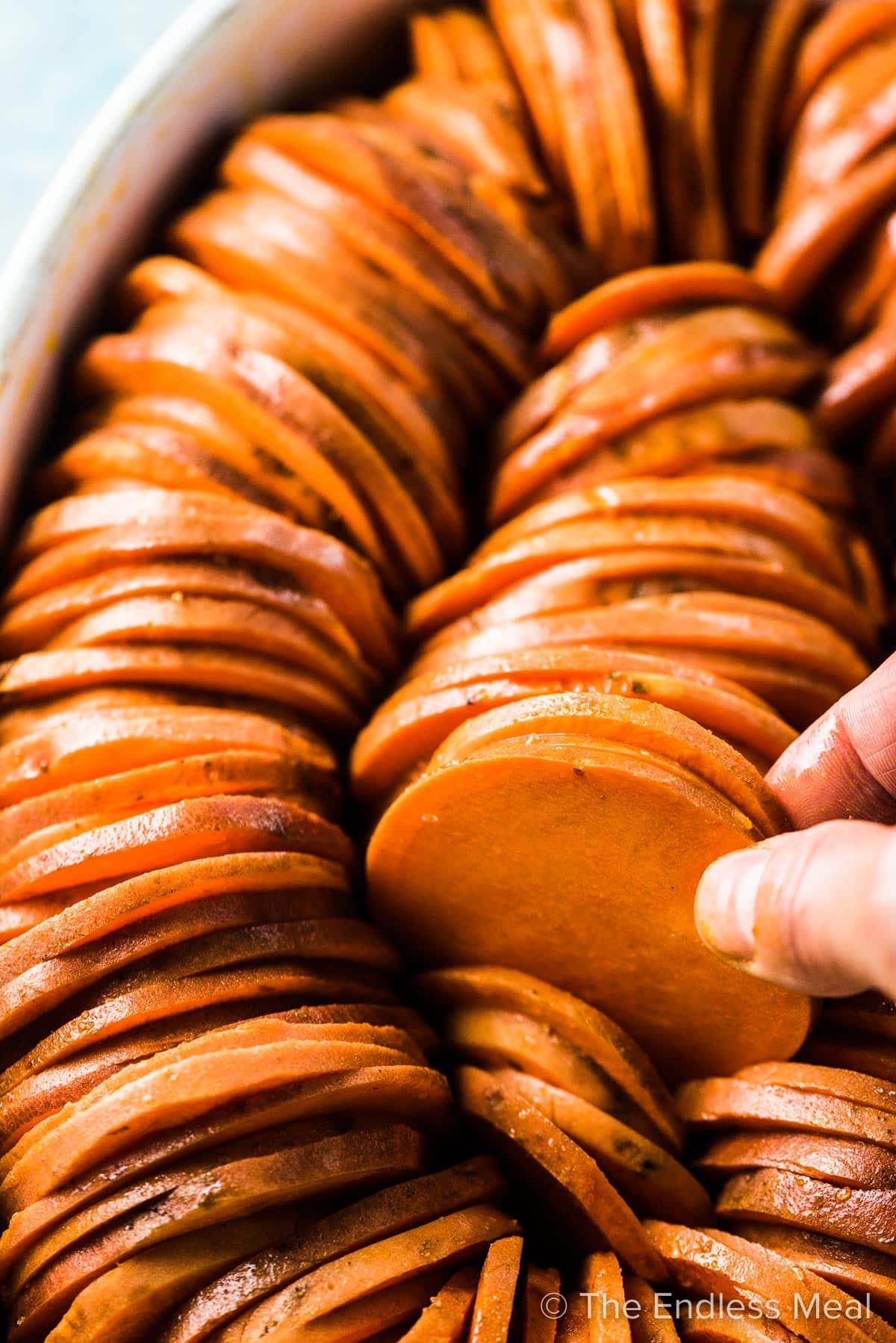 A hand assembling this shingled sweet potato casserole.