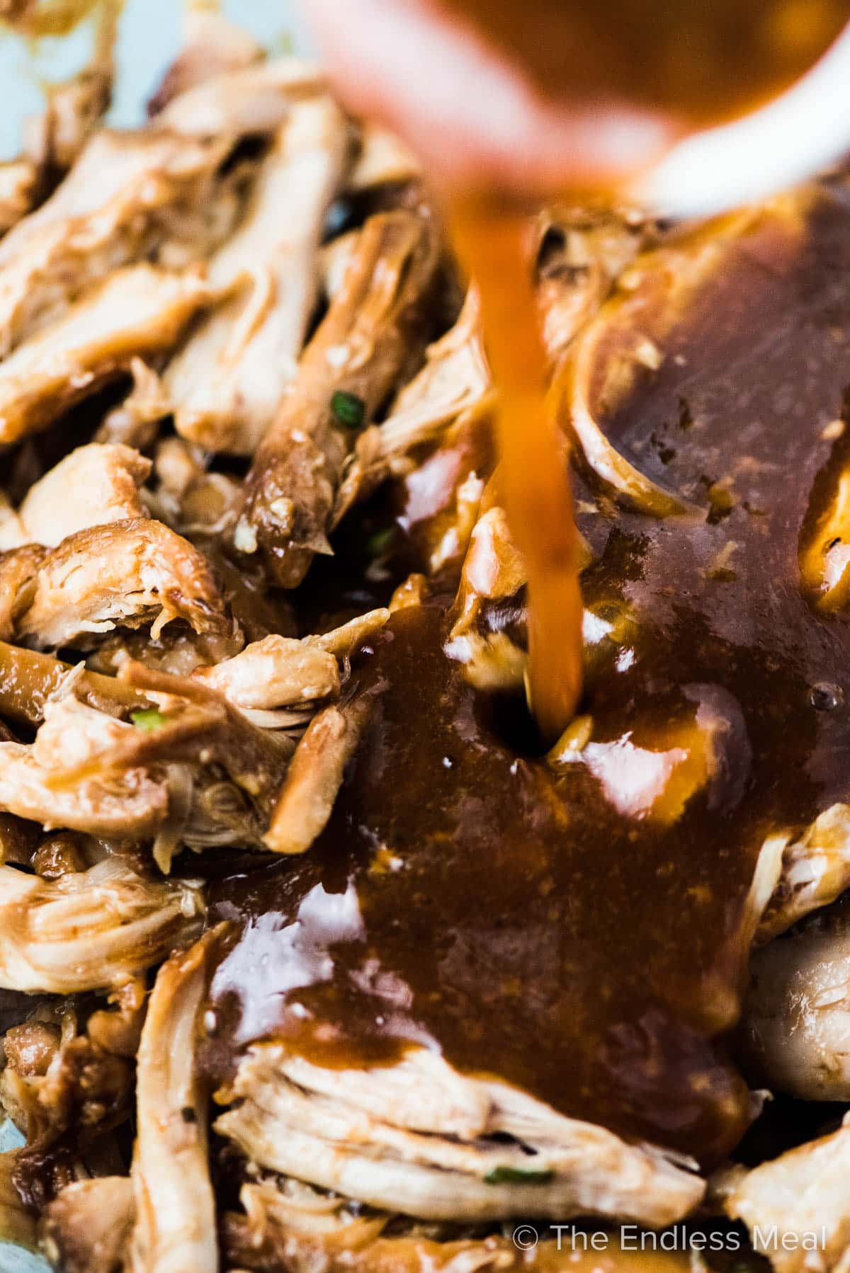 Slow cooked shredded chicken with honey garlic sauce being poured over the top.