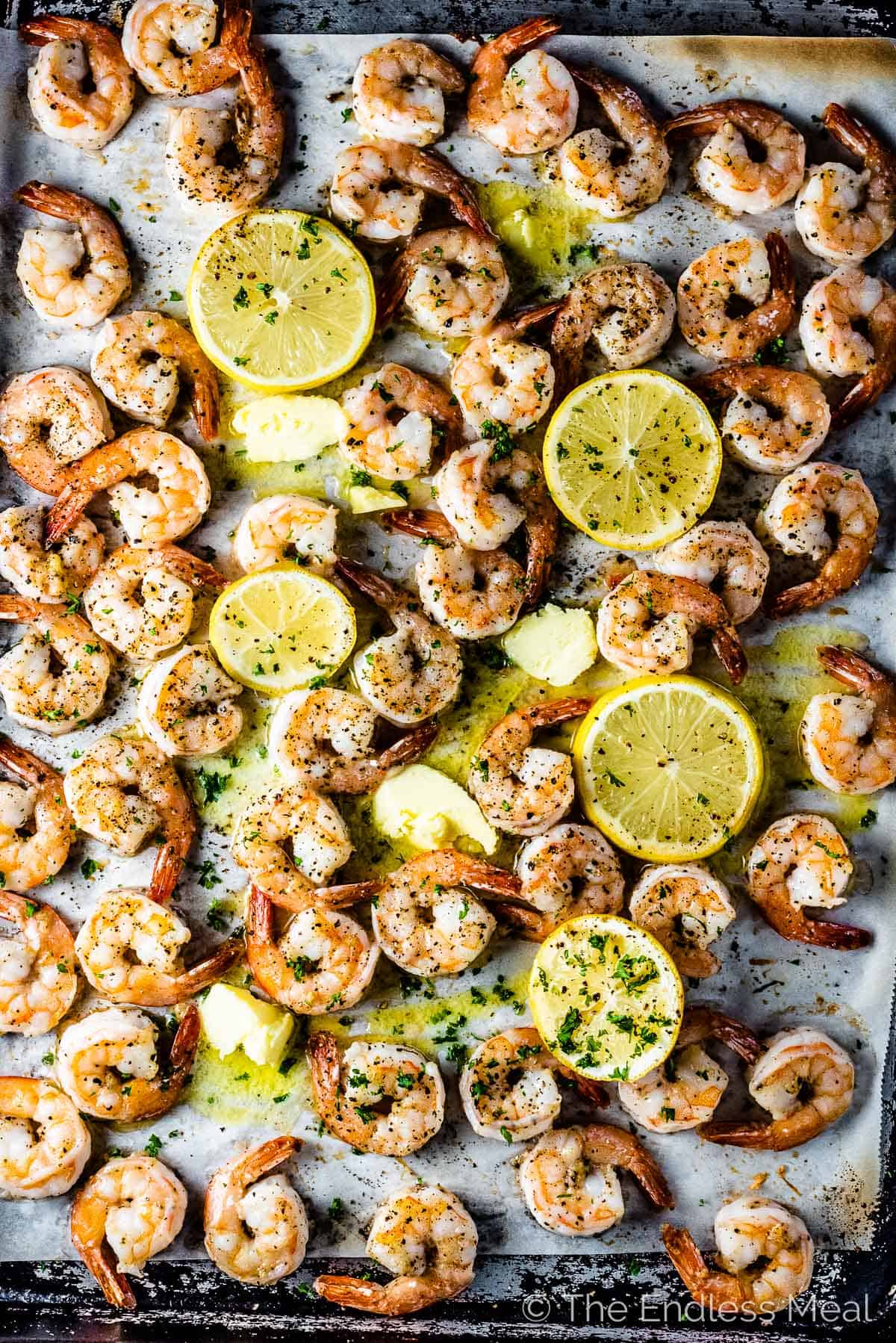 A tray of baked shrimp with slices of lemon.
