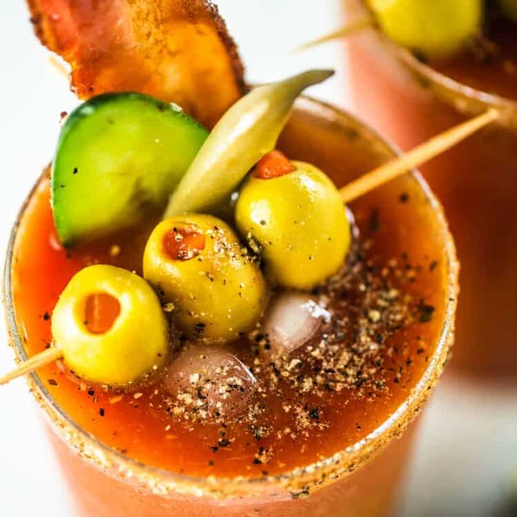 A close up of the best Bloody Caesar drink with olives, bacon, pickled bean, and cucumber as garnish.