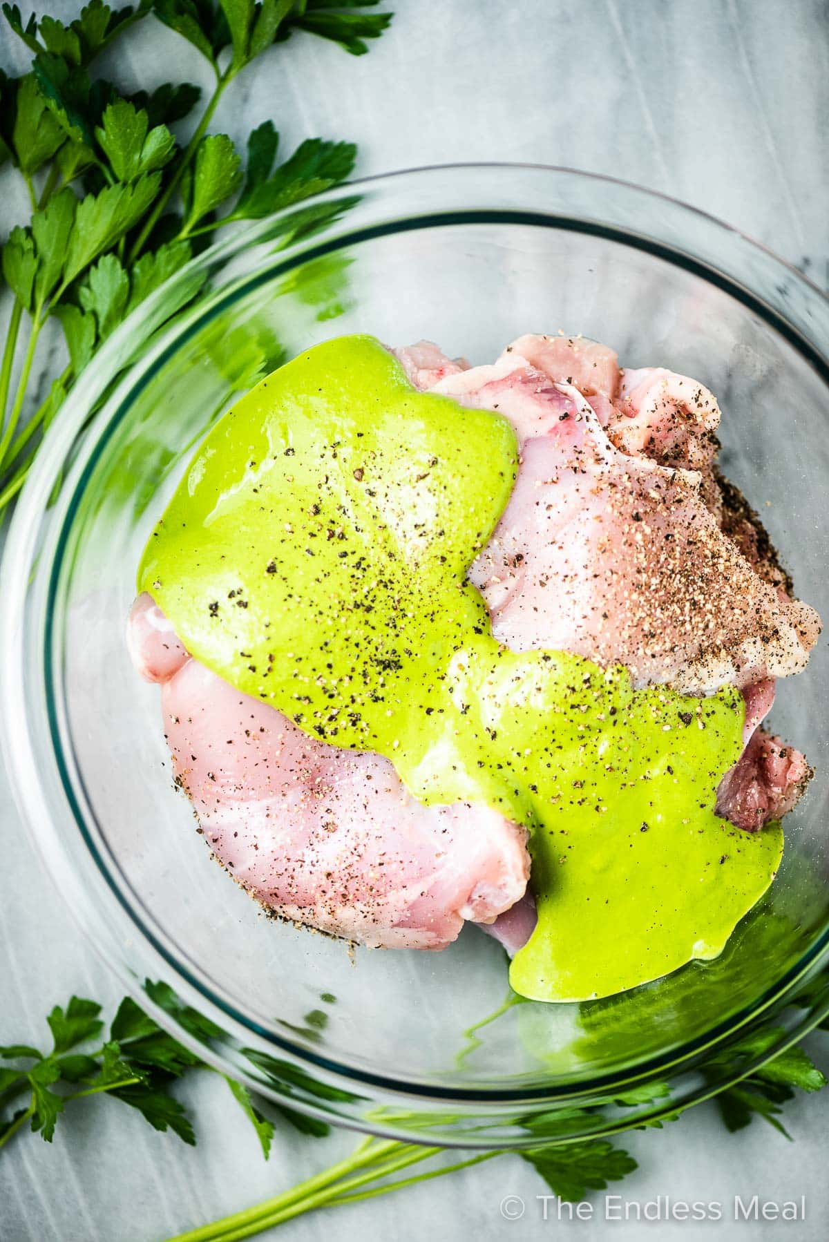 Chicken thighs in a bowl marinating in green goddess dressing.