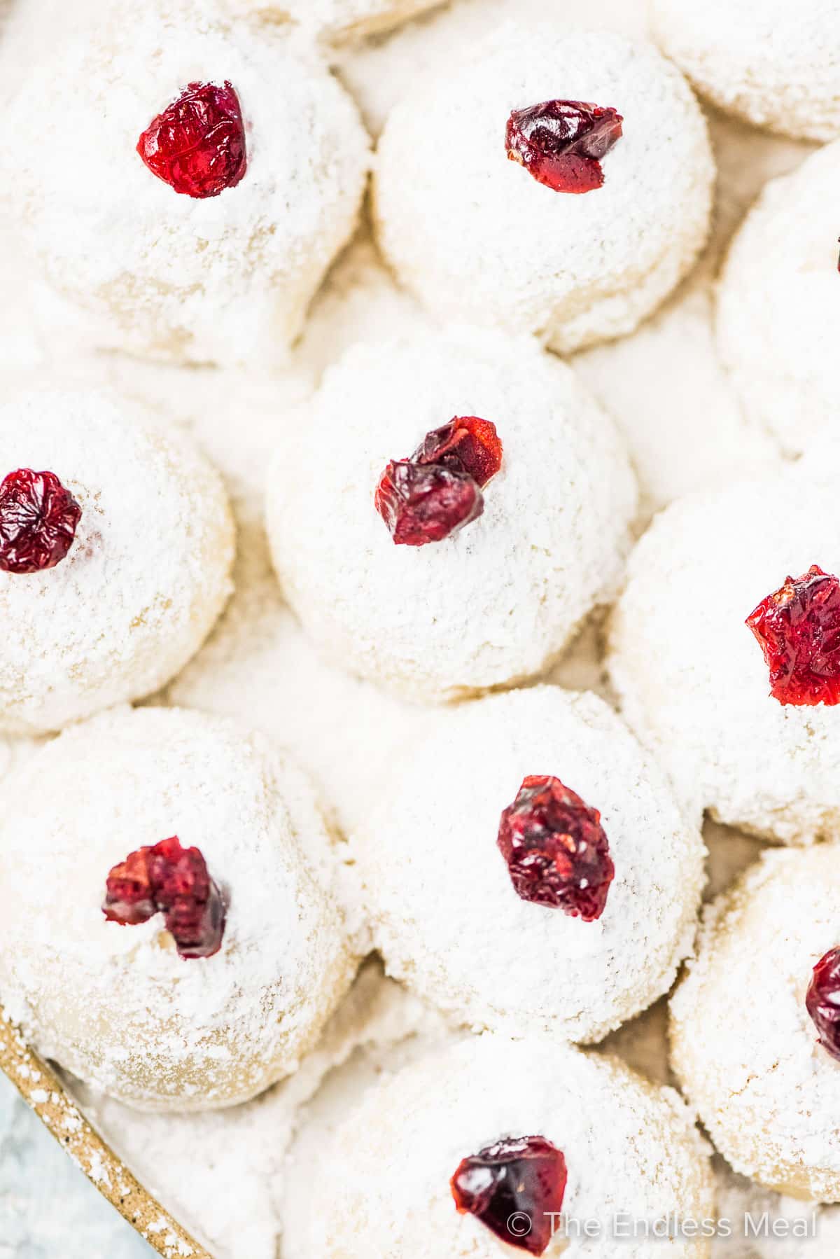 Looking down on a plate of snowball keto christmas cookies topped with cranberries.
