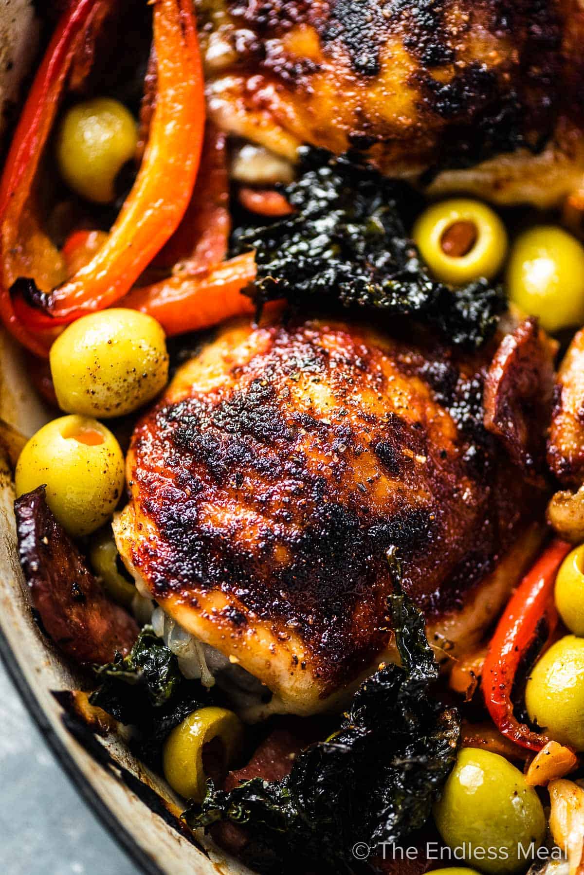A close up of a this Spanish chicken bake with olives, kale, peppers, and chorizo.