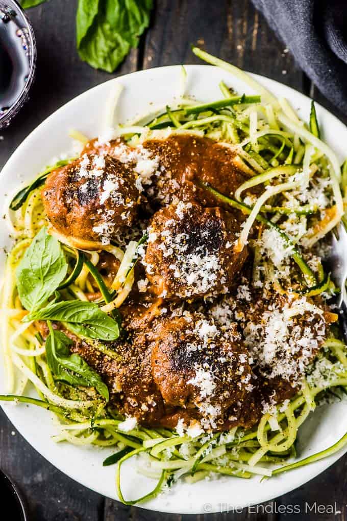 A white plate full of zucchini noodles, pasta sauce, and meatballs