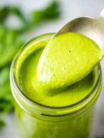 A spoon taking a scoop out of a jar of healthy green goddess dressing;