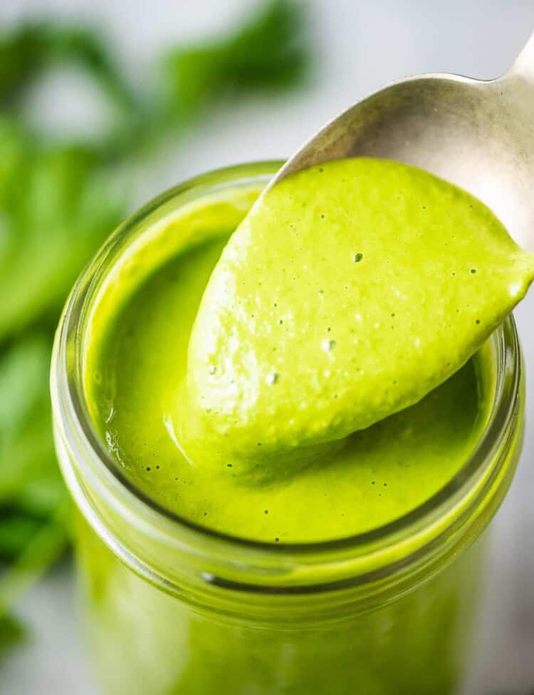 A spoon taking a scoop out of a jar of healthy green goddess dressing;