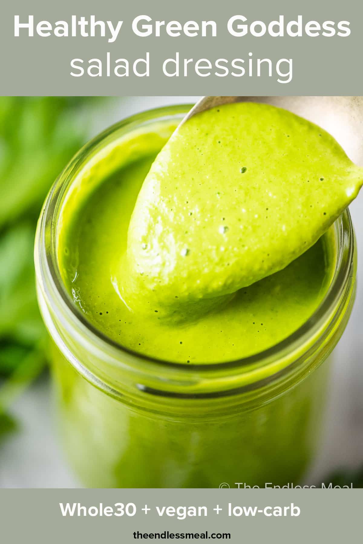 A spoon taking a scoop out of a jar of healthy green goddess dressing and the recipe title on top of the picture.