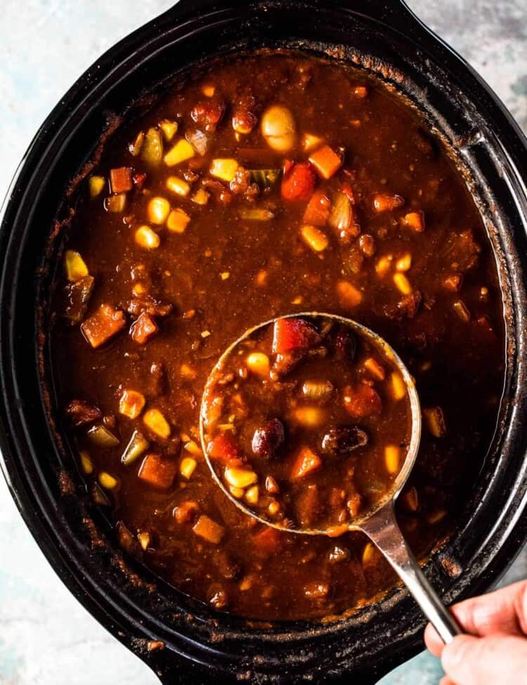 Looking down on vegetarian chili in a slow cooker with a ladle taking a scoop.