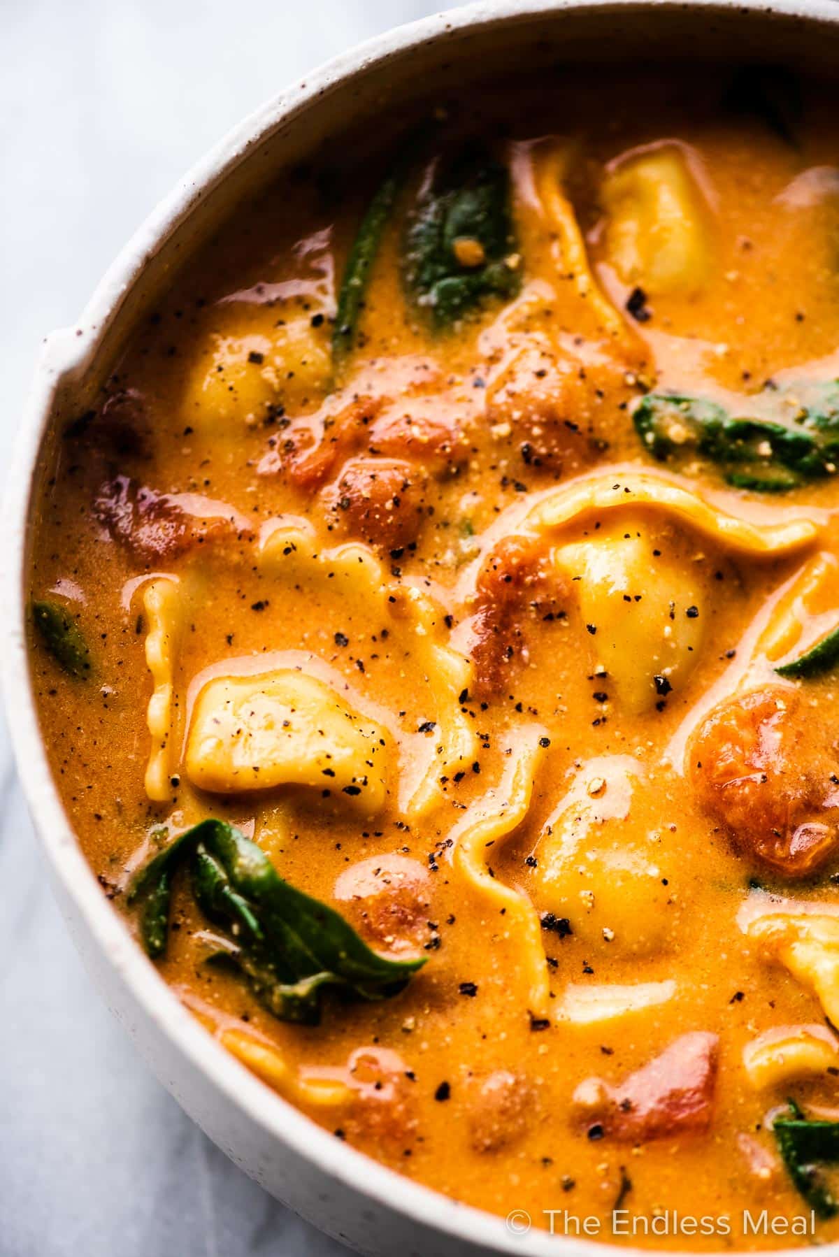 A bowl of cashew creamy tortellini soup with spinach.
