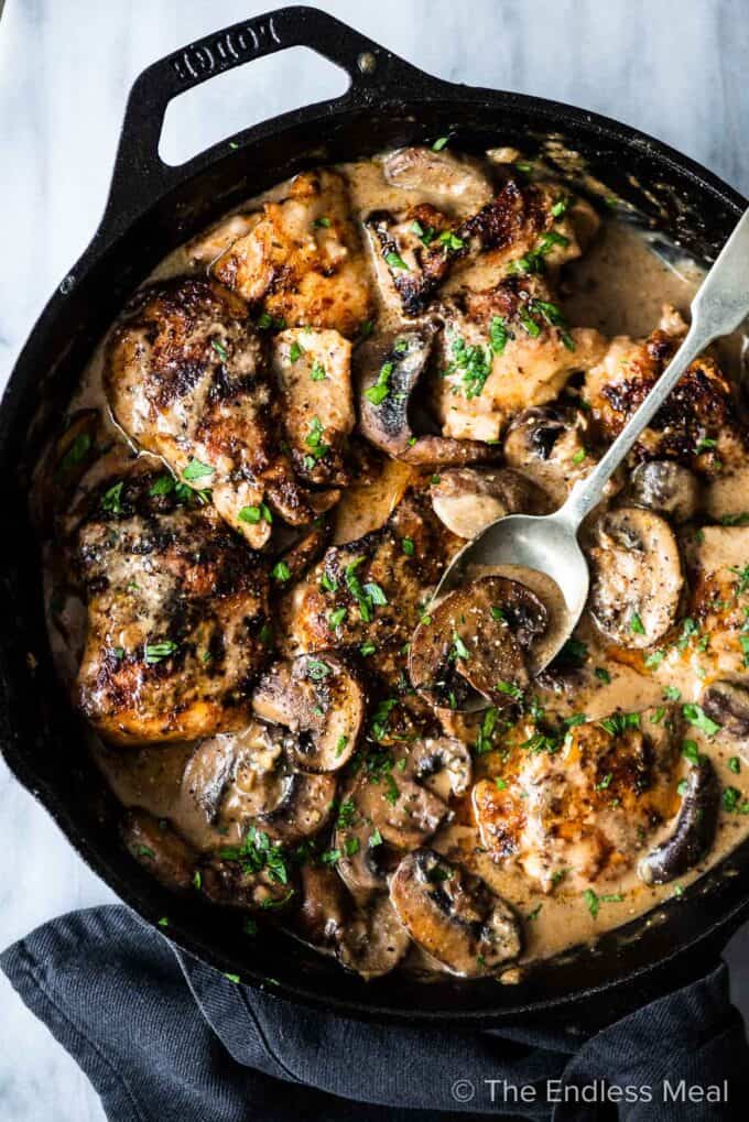 This creamy mushroom chicken recipe in a cast iron pan with a spoon in it.