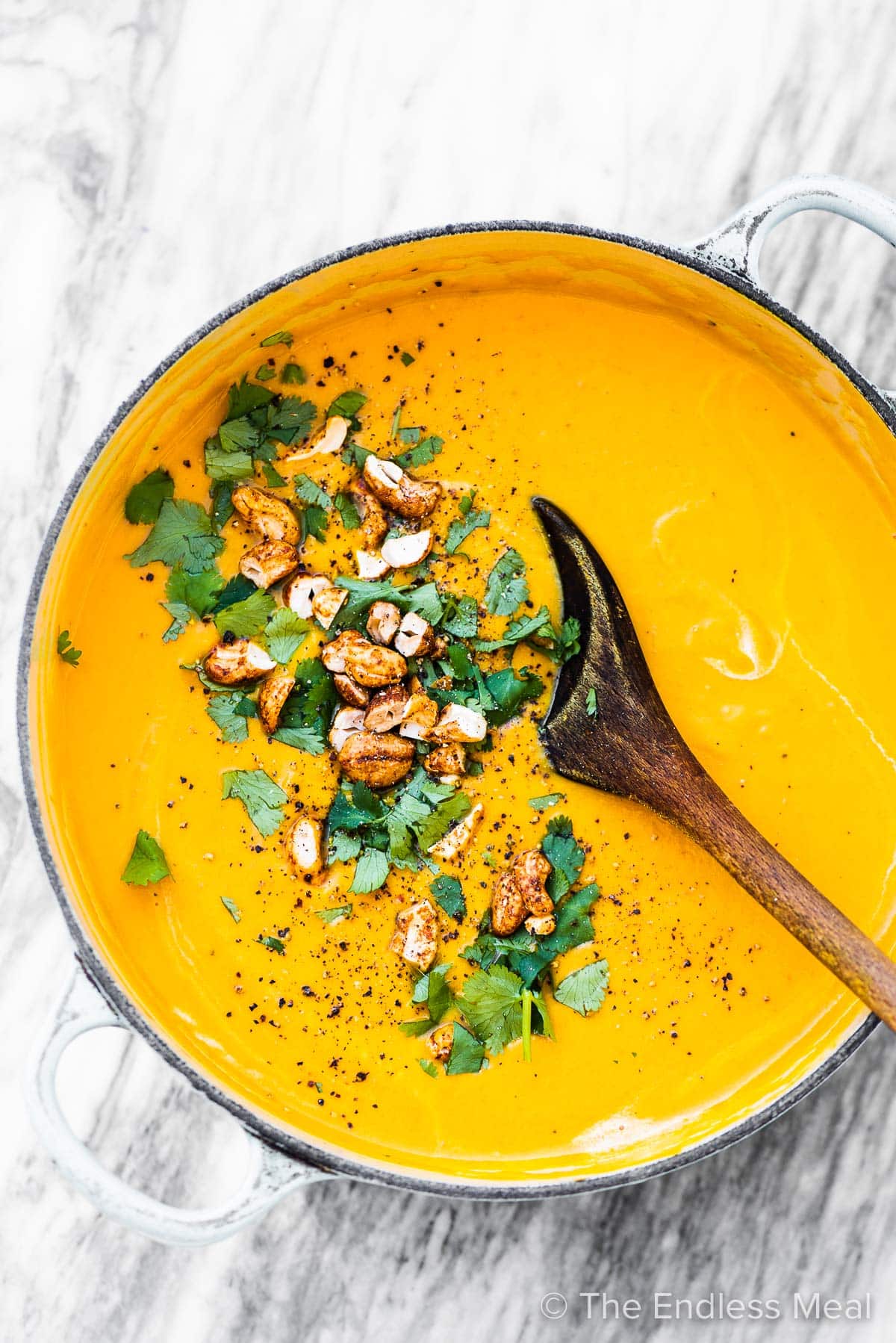 A pot of carrot soup with cashews and cilantro on top.