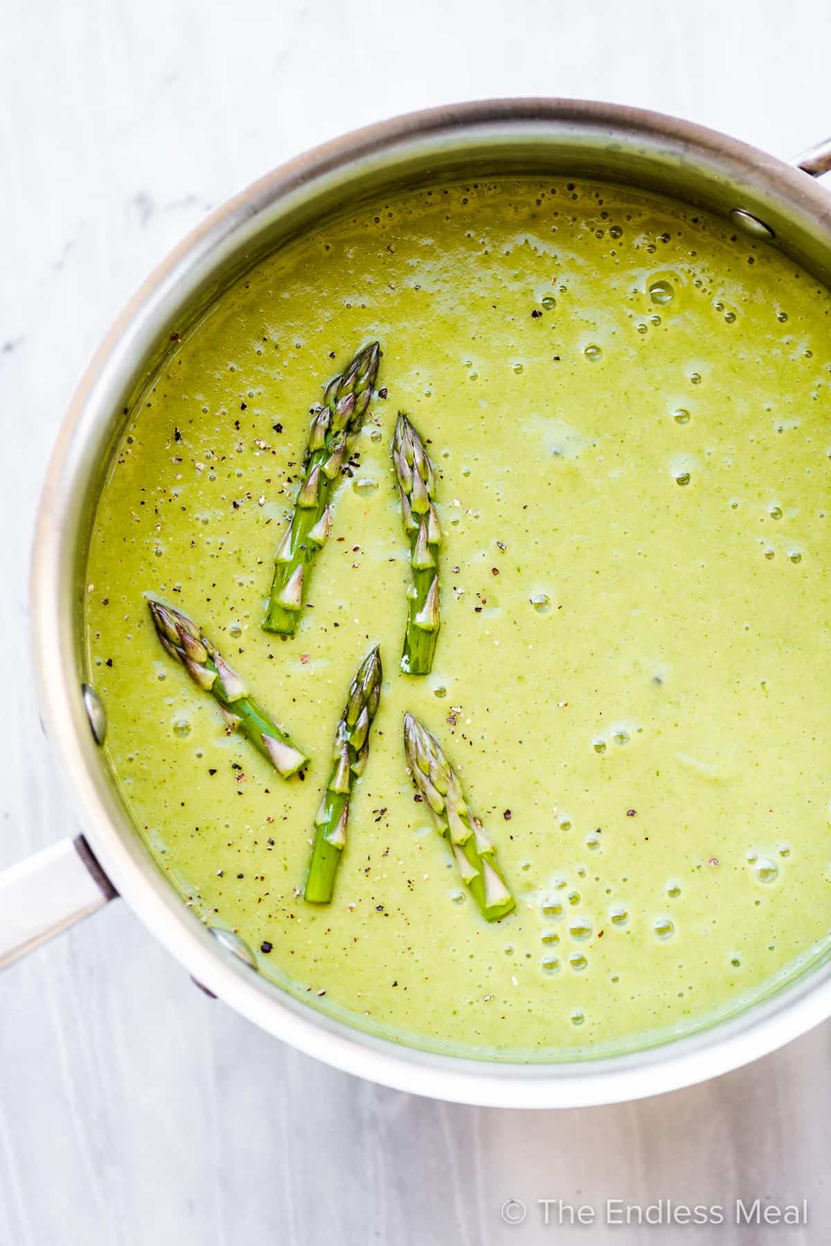 Asparagus soup in a pot with asparagus spears on top.