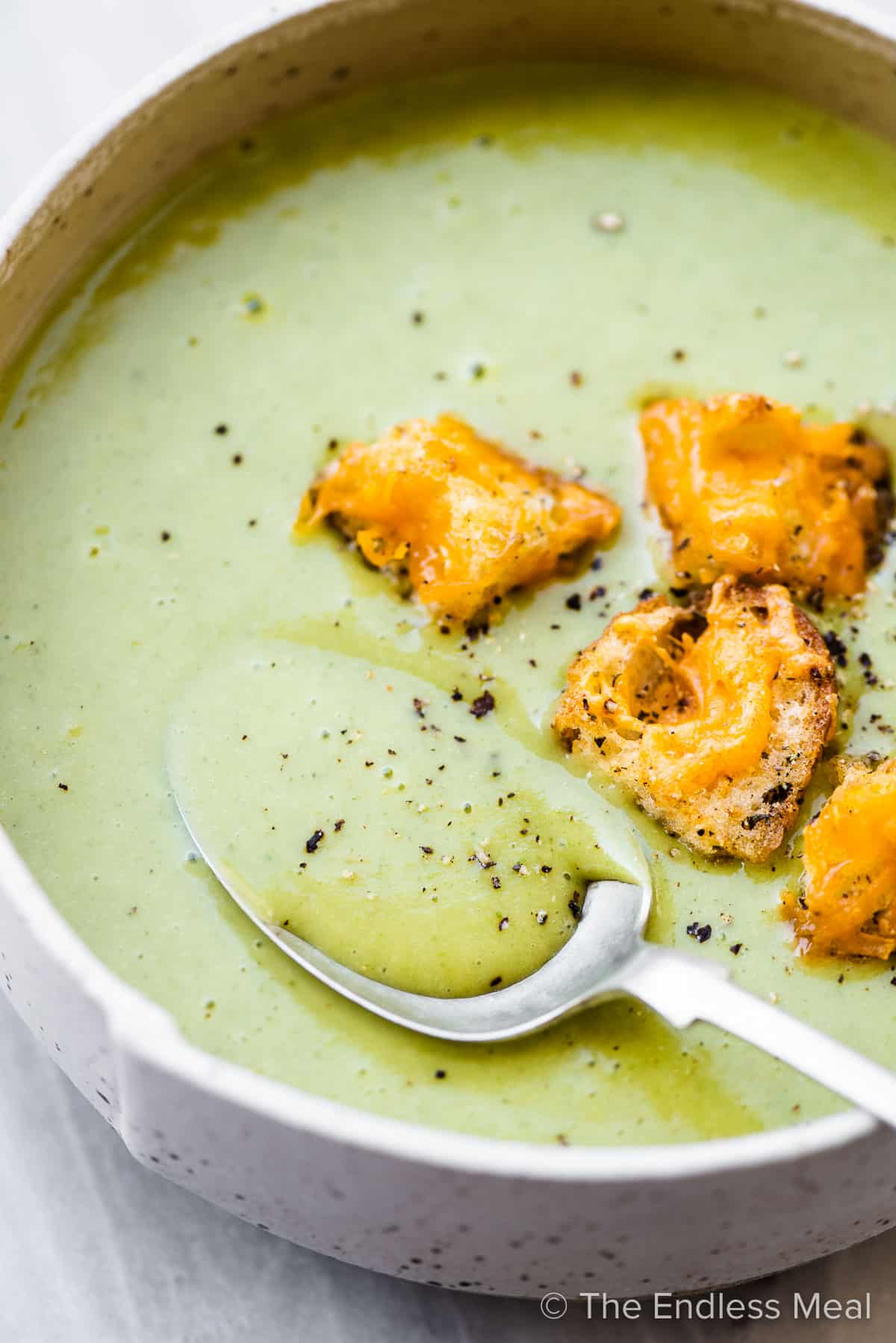 Side view of a bowl of asparagus soup with cheesy croutons and a spoon.