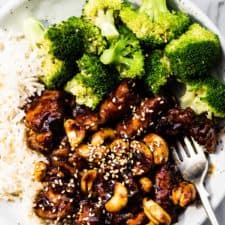 Cashew chicken on a plate with rice and steamed broccoli.