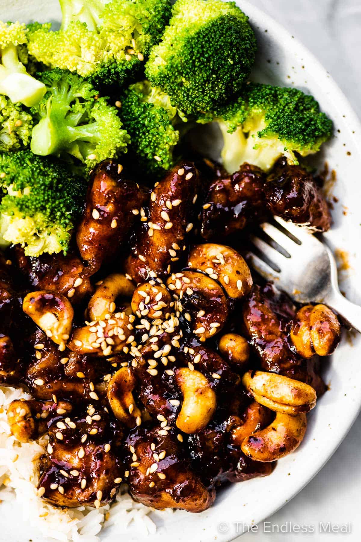 A close up of cashew chicken on a plate with steamed broccoli.