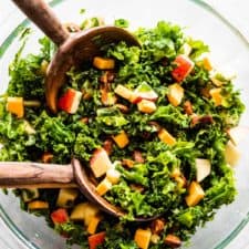 Kale apple salad in a bowl with wooden salad tongs.