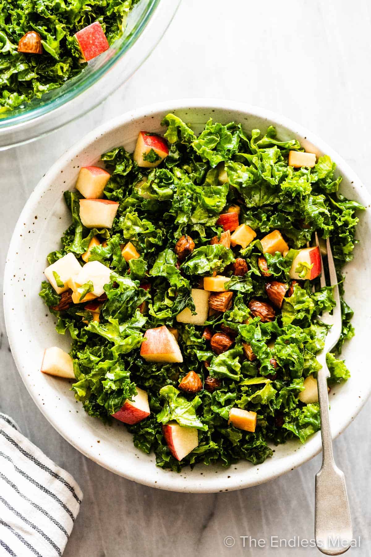 Kale and apple salad in a bowl with a fork inside.