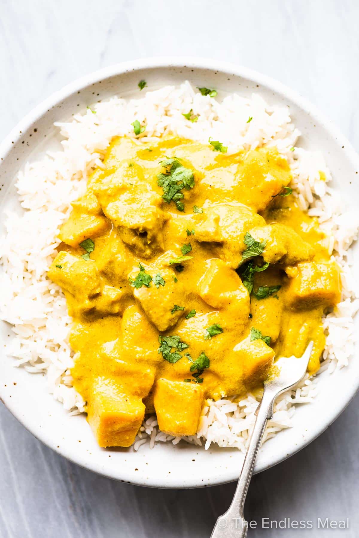 A white bowl with mango chicken curry on rice and a fork in it.
