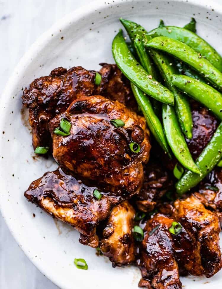 Soy sauce chicken on a white plate with snap peas.